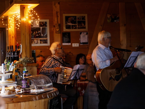 Live Musik bei einer Firmenweihnachtsfeier im Christbaumdorf Mittelsinn Musiker spielen Gitarre und Akkordeon in einer Holzhütte bei einer Weihnachtsfeier