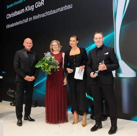 Christbaum-Klug erhält Taspo Award für Nachhaltigkeit Fünf Personen stehen auf einer Bühne bei der Preisverleihung, eine Frau hält einen Blumenstrauß in der Hand